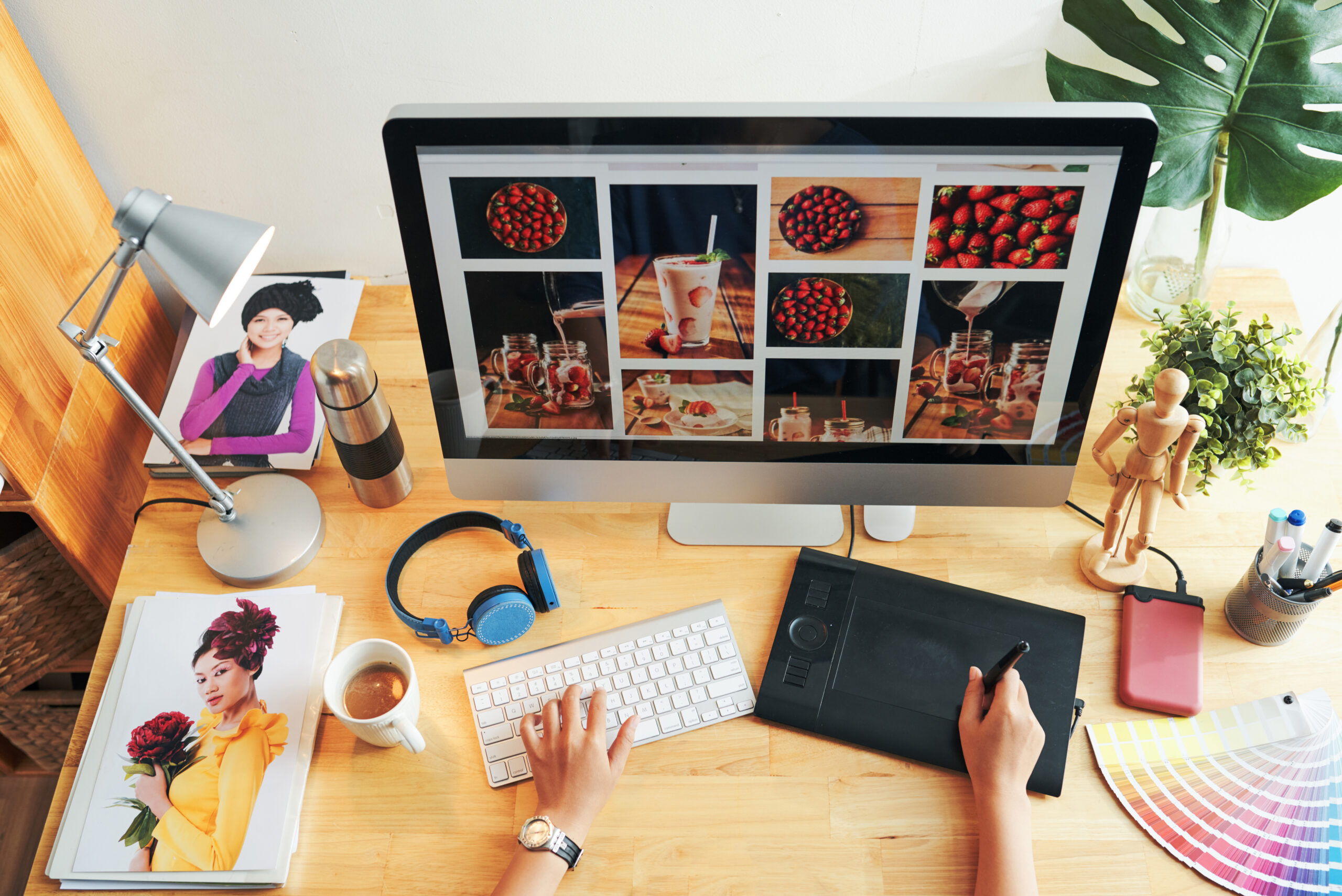Directly above view of unrecognizable designer choosing photos for magazine page on modern computer in office